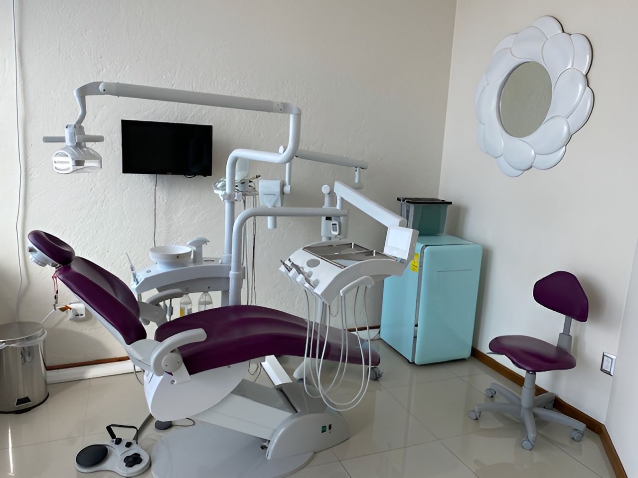 Sala de examen dental con silla y equipo de color violeta; un espejo en forma de flor cuelga en la pared.