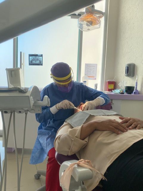 Un dentista con uniforme azul, visera y guantes examina a un paciente en una silla dental.