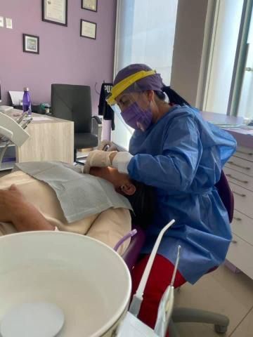Dentista con equipo de protección realizando un procedimiento dental en un paciente en un consultorio médico.