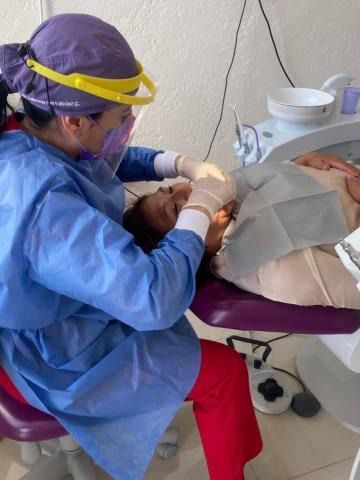 Dentista con equipo de protección examinando la boca de un paciente en un consultorio dental.