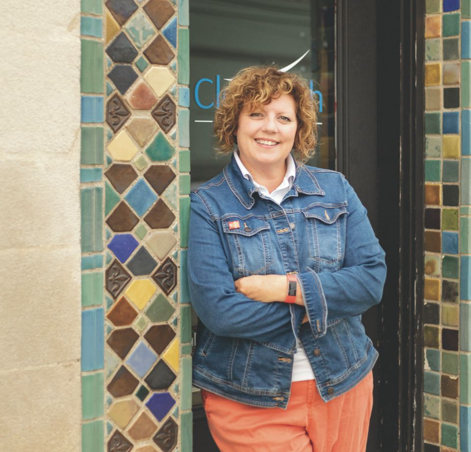 Mindy in jean jacket, arms crossed, leaning against colorful tiled doorway.