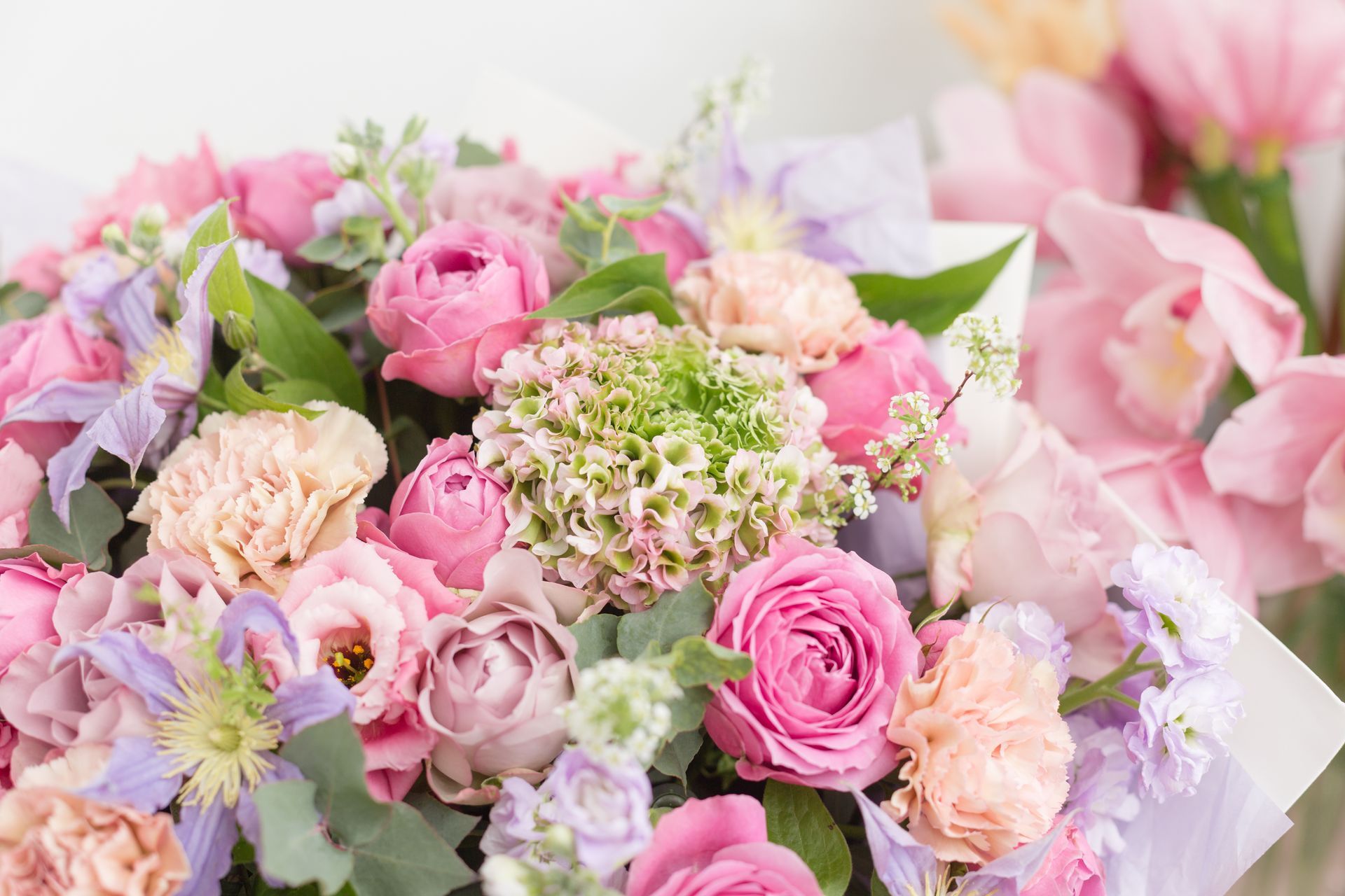 A dense, colorful bouquet featuring various shades of pink roses, light purple flowers, and green hydrangea blooms.