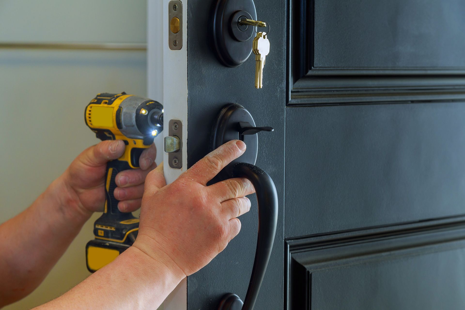 Person using a yellow drill to install a black door handle on a black door.