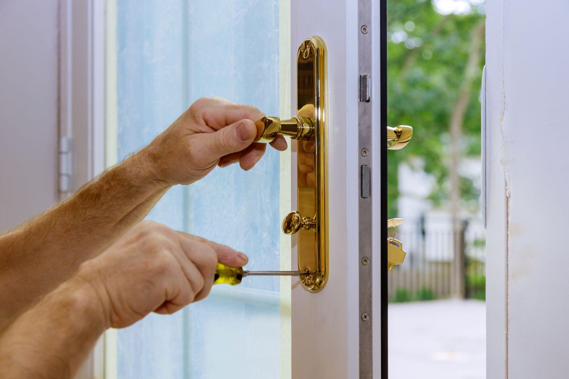 Hands using a screwdriver to install a gold door handle on a white door.