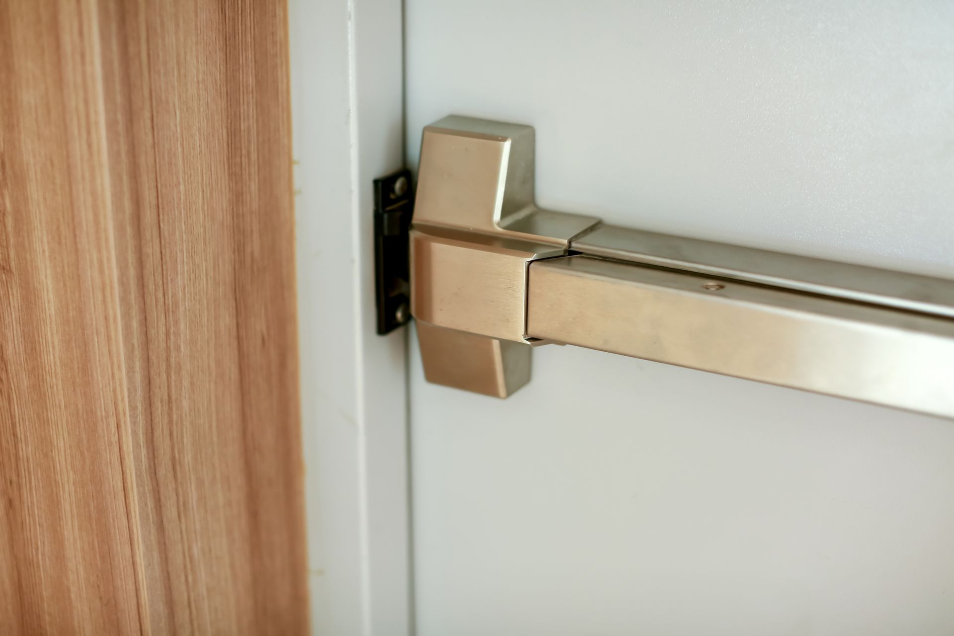 Silver push bar door handle on a white door, mounted next to a wood panel.