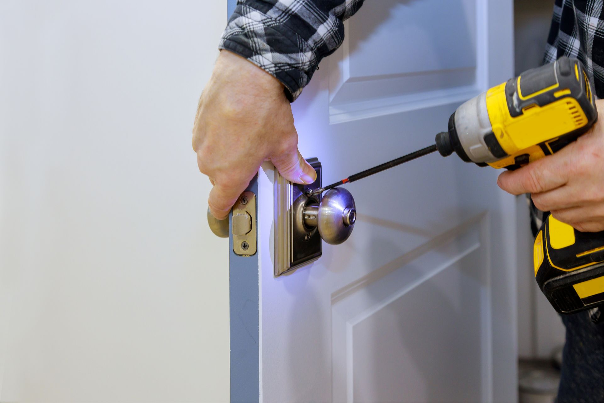 Person using a yellow power drill to install a doorknob on a white door.