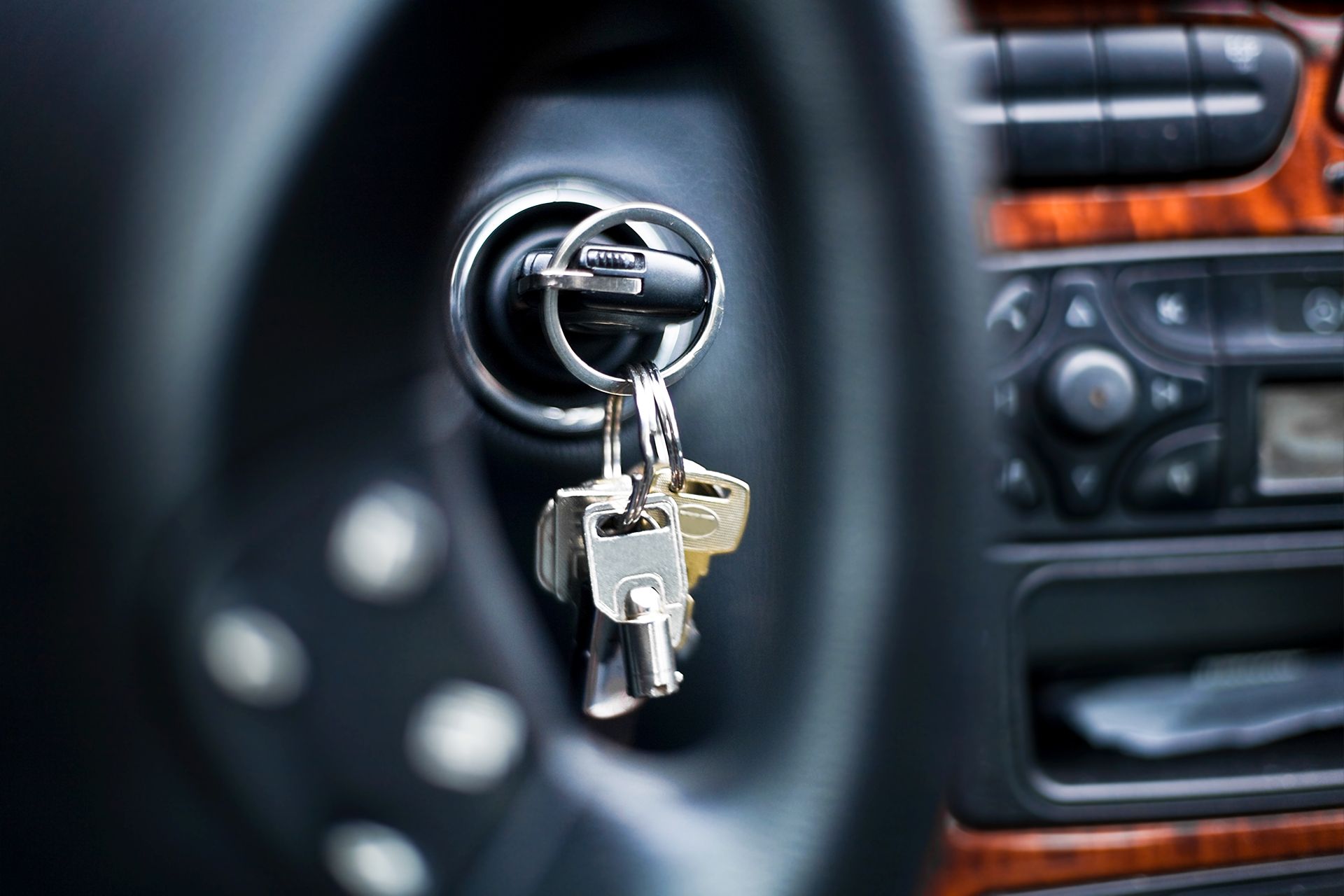 Keys in a car's ignition, attached to a ring. Steering wheel and dashboard visible in the background.