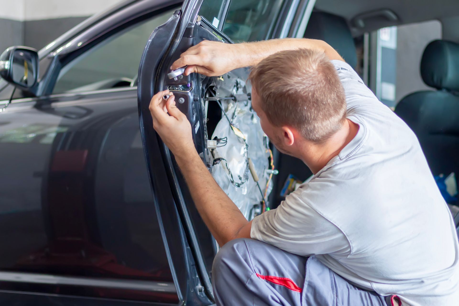 A mechanic working on a car door in a garage.