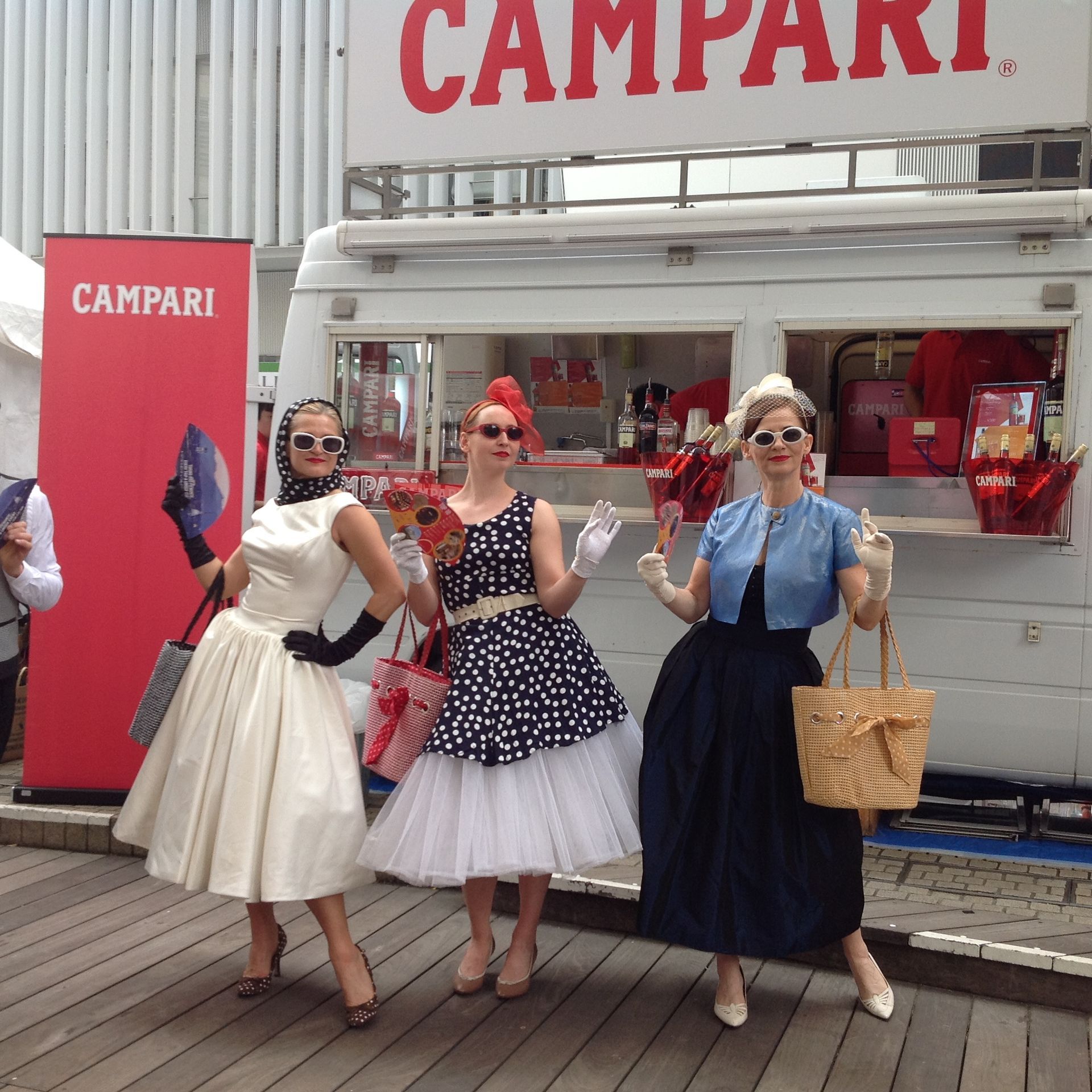 Tre donne in piedi davanti a un cartello Campari