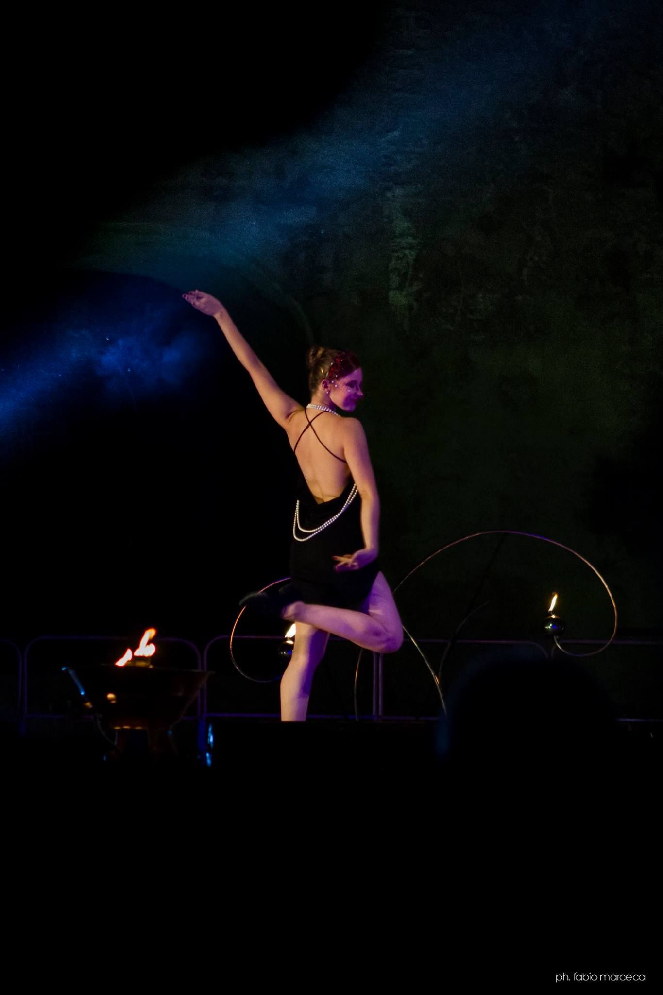 Una donna con un abito nero balla con i cerchi su un palco.