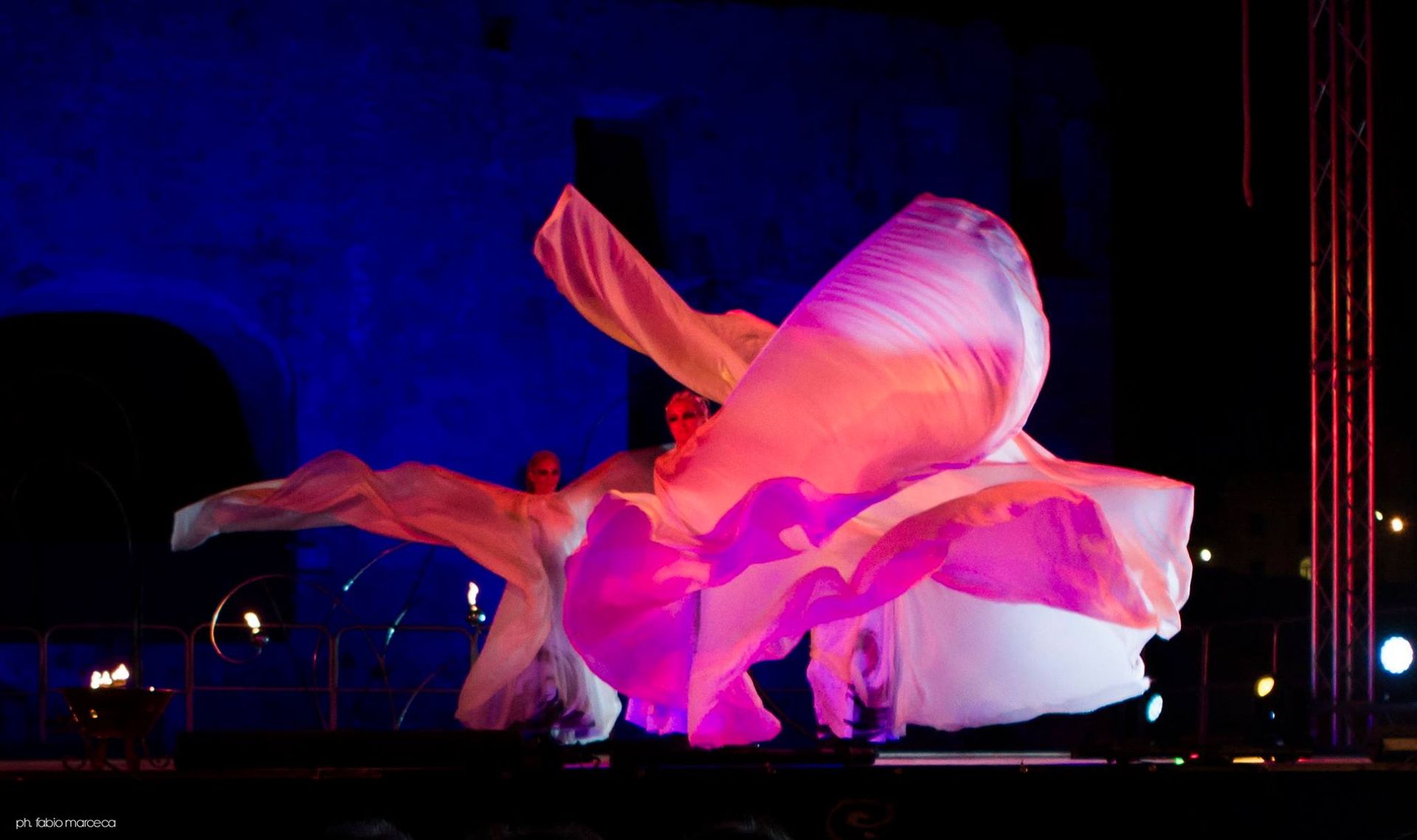 Una donna vestita di bianco sta ballando su un palco con luci viola dietro di lei.