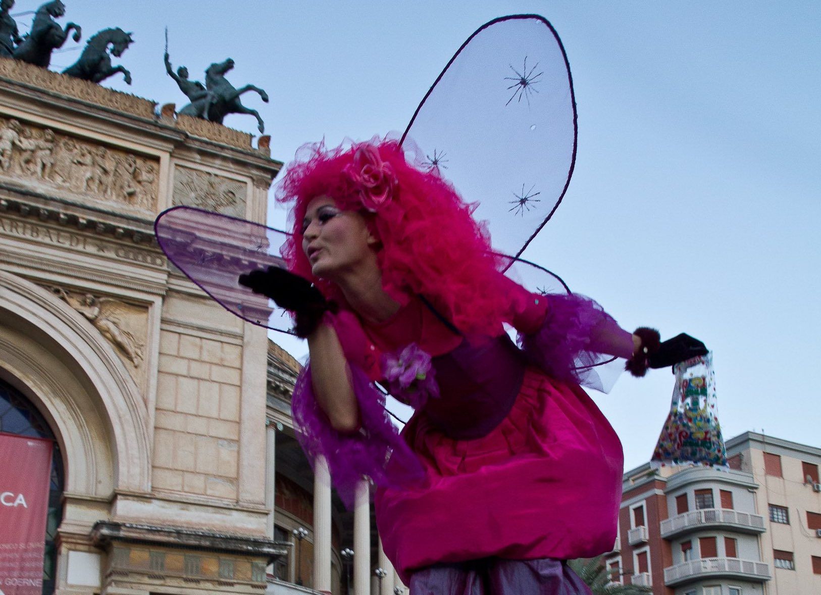 Una donna in un costume da fata rosa cammina sui trampoli