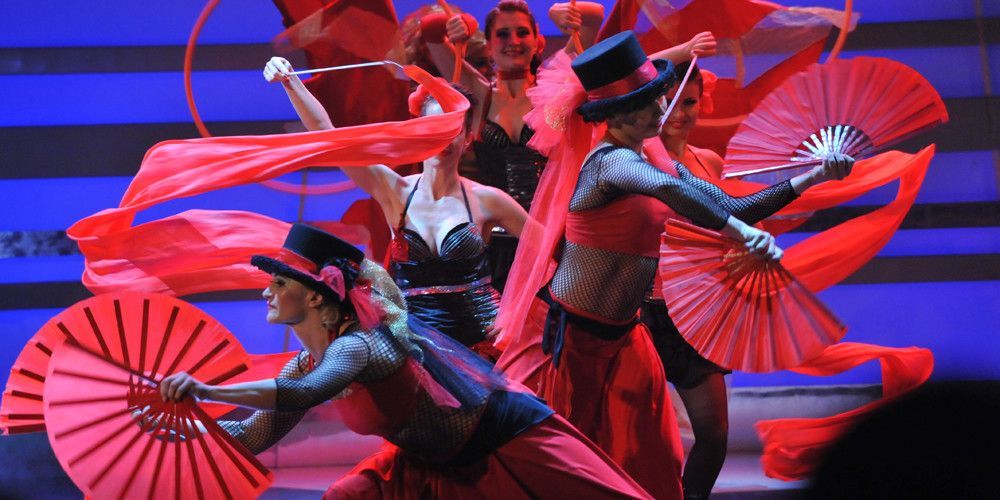 Un gruppo di persone sta ballando su un palco con dei ventagli rossi.