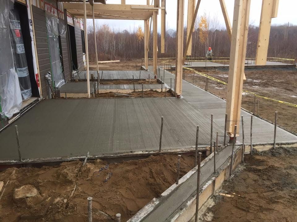 Une passerelle en béton est en cours de coulage devant un bâtiment en construction.