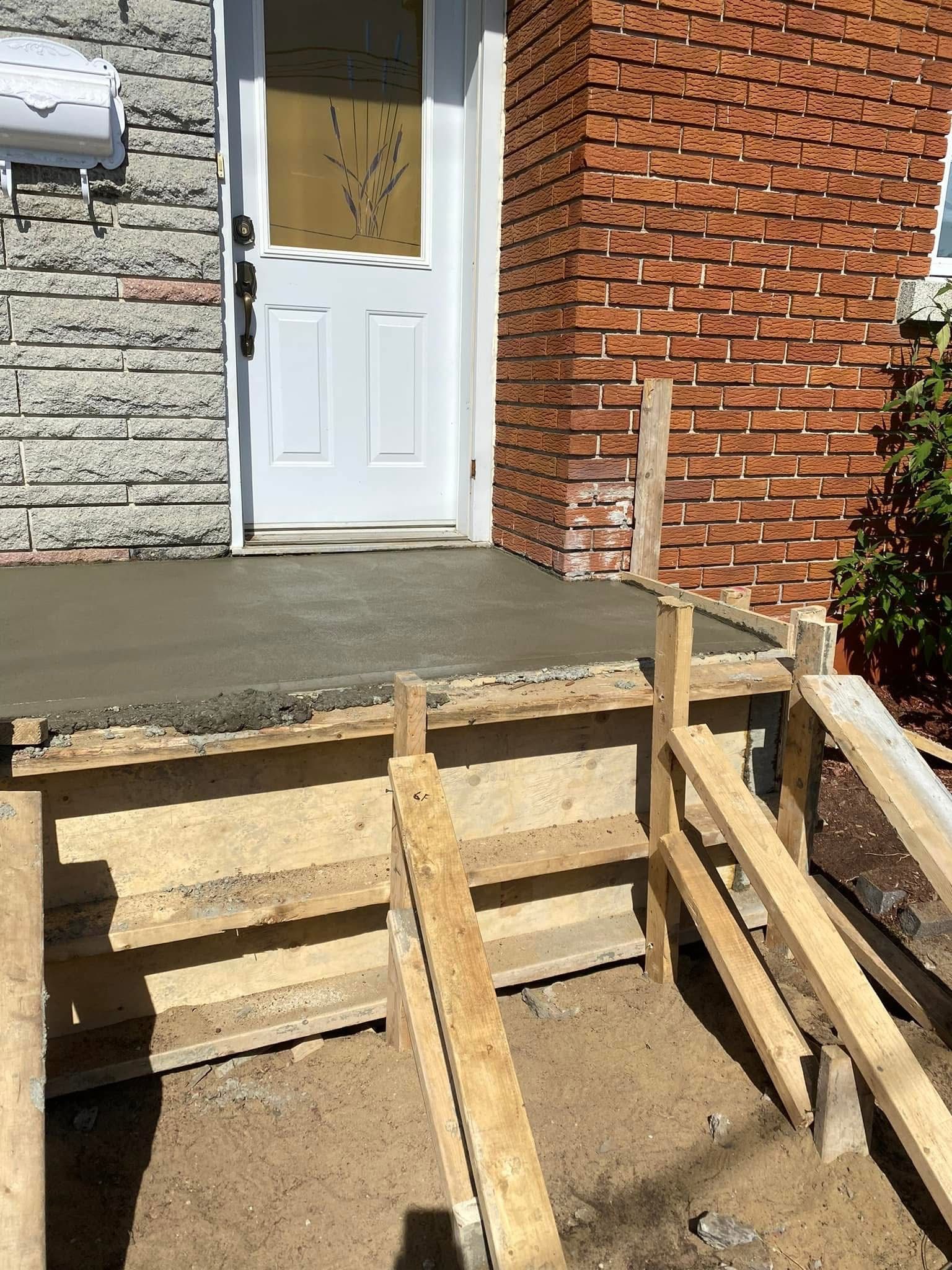 Un porche en béton est en cours de construction devant une maison en briques.