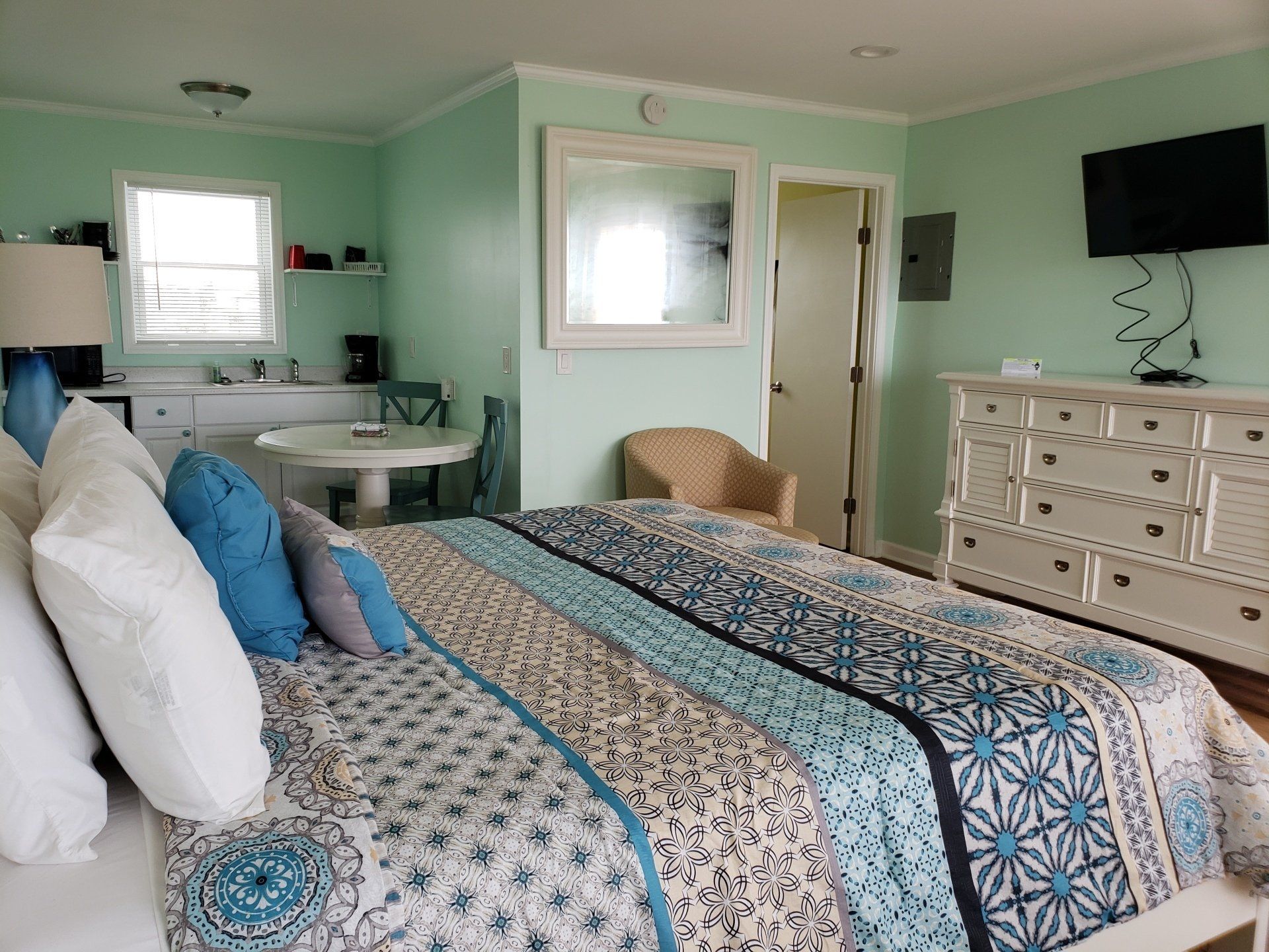 A bedroom featuring a bed with a blue and white patterned quilt, mint green walls, a white dresser, and a small table.