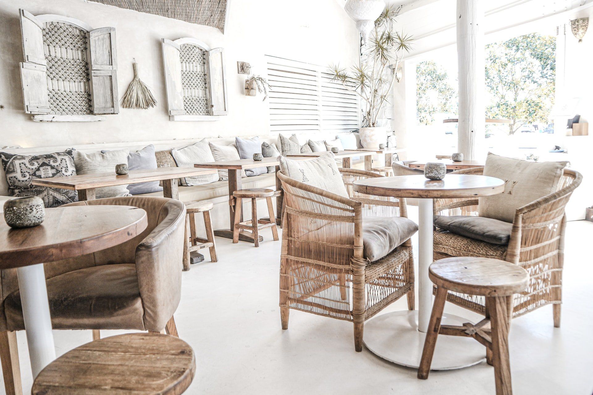 A bright, airy restaurant interior with white walls, wicker chairs, round tables, and neutral-toned decor.