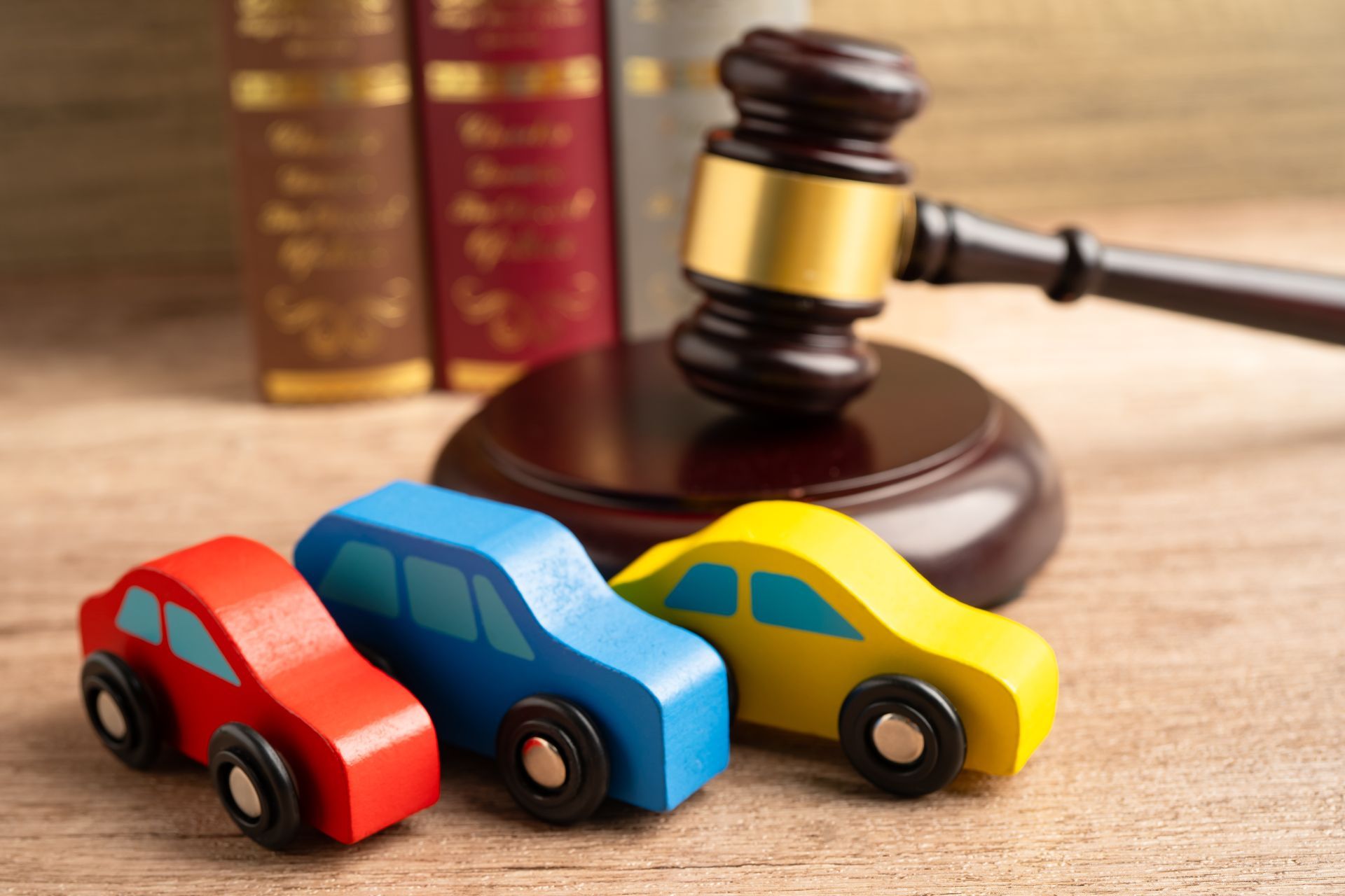 Colorful wooden toy cars arranged beside a judge’s gavel and law books on a desk.
