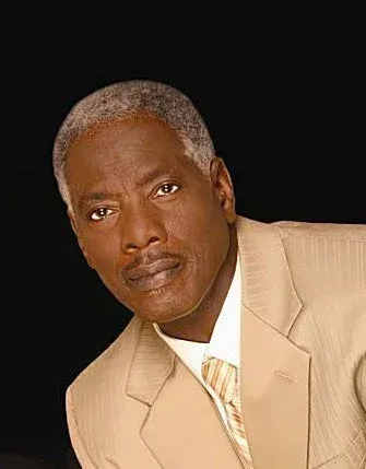 Singer, Lee Williams in a tan suit and tie is looking at the camera.