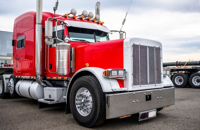 Red and white semi-truck parked outdoors, with chrome detailing, on a cloudy day.