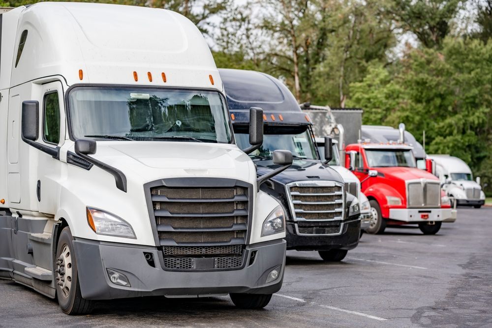 Semi-trucks parked in a row on asphalt; white, black, and red trucks in a lot.