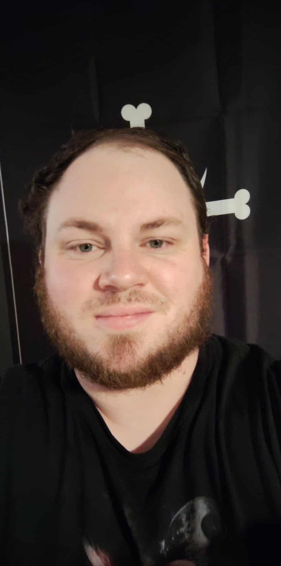 A man with a beard and a black shirt, smiling, with bone decorations on a black background.