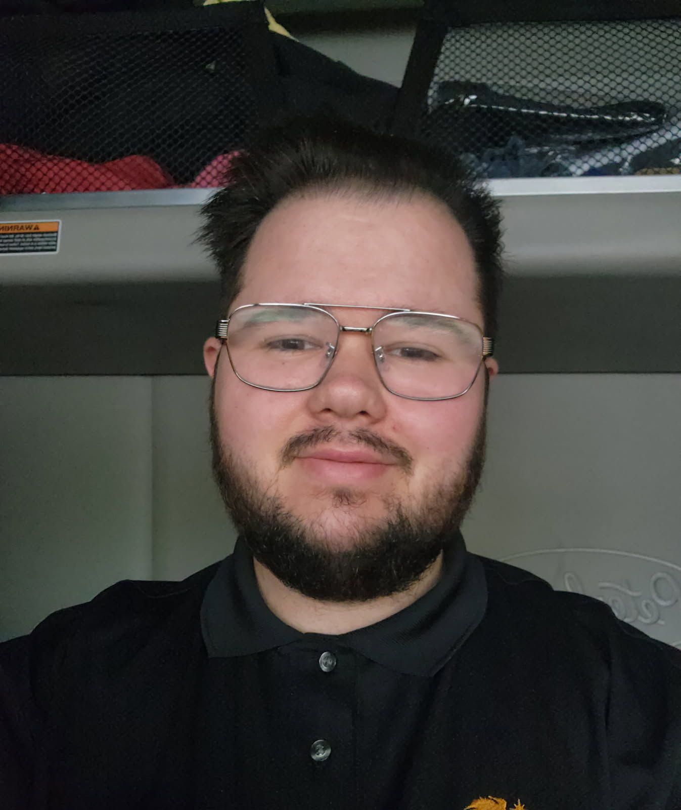 Man with glasses and beard in black polo shirt, smiling.