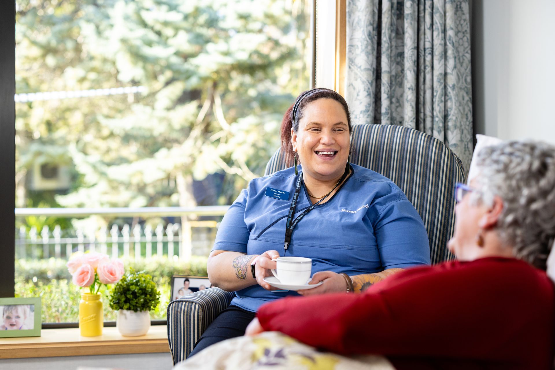 A nurse is sitting in a chair talking to an elderly woman.