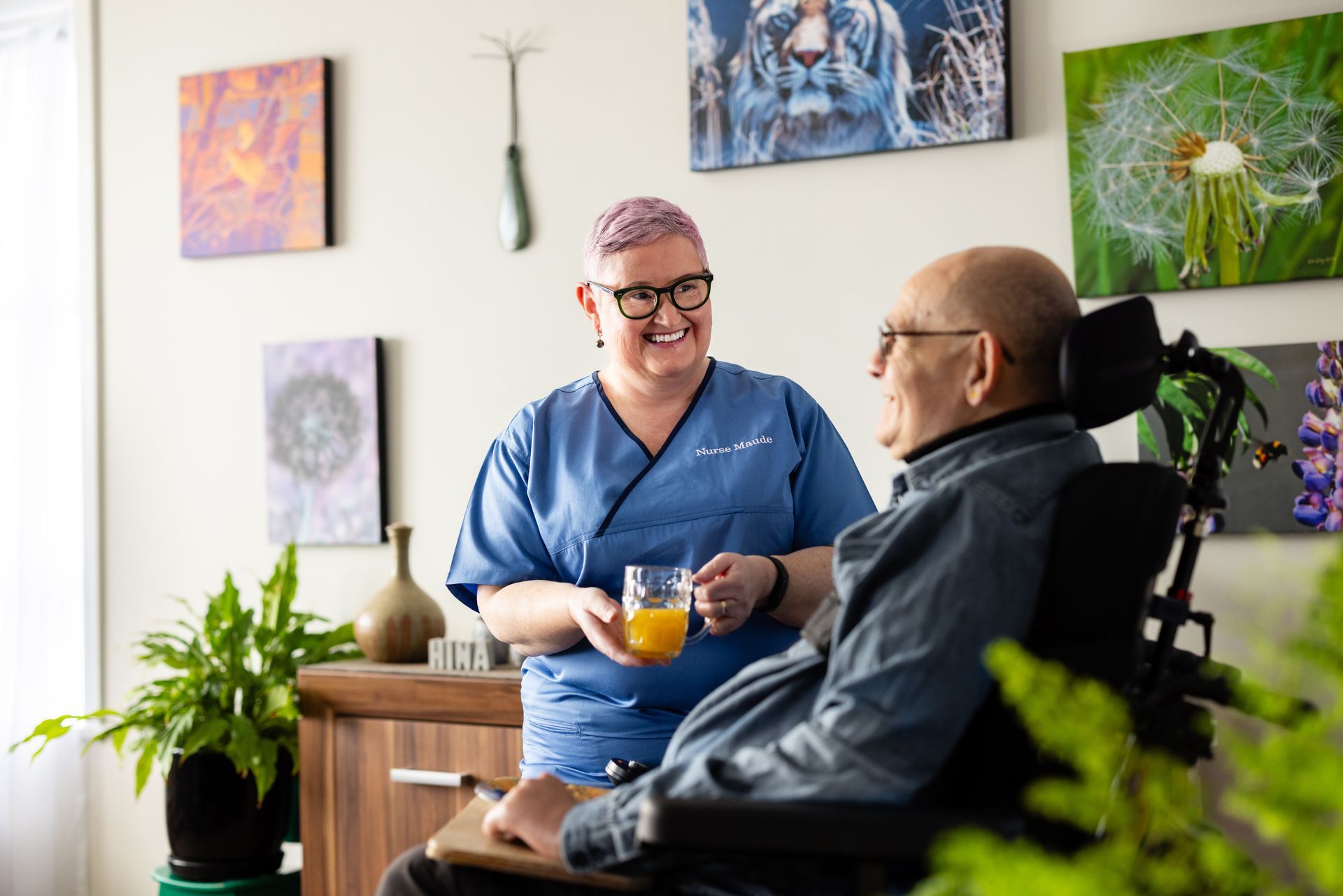 A nurse is holding a cup of orange juice next to a man in a wheelchair.