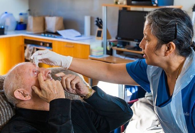 A nurse is giving an elderly man a pill in his mouth.