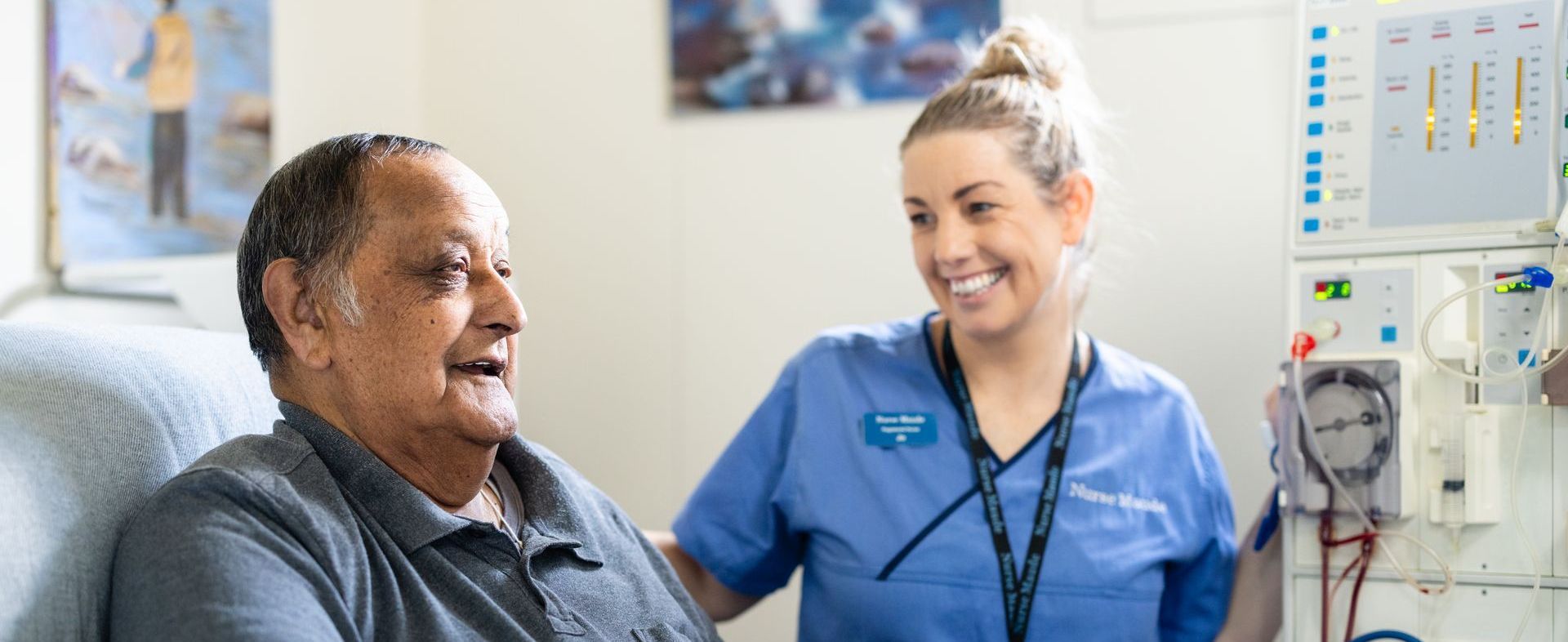 A woman in a blue scrub is smiling and holding a clipboard