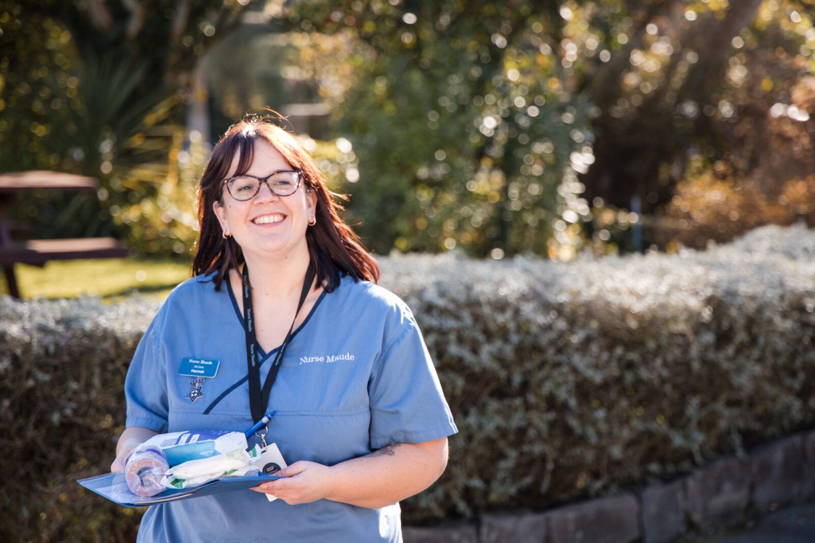 A woman in a blue scrub is smiling and holding a clipboard