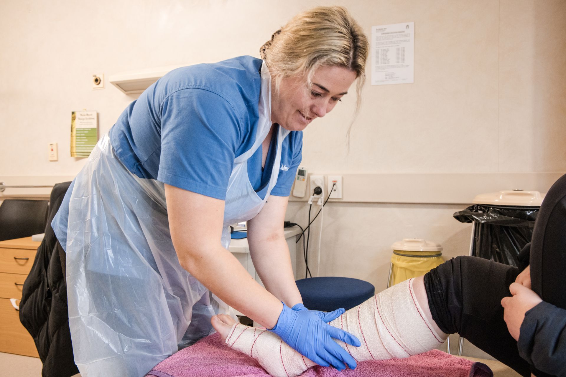 A woman wearing a blue, white apron and blue gloves dressing wound