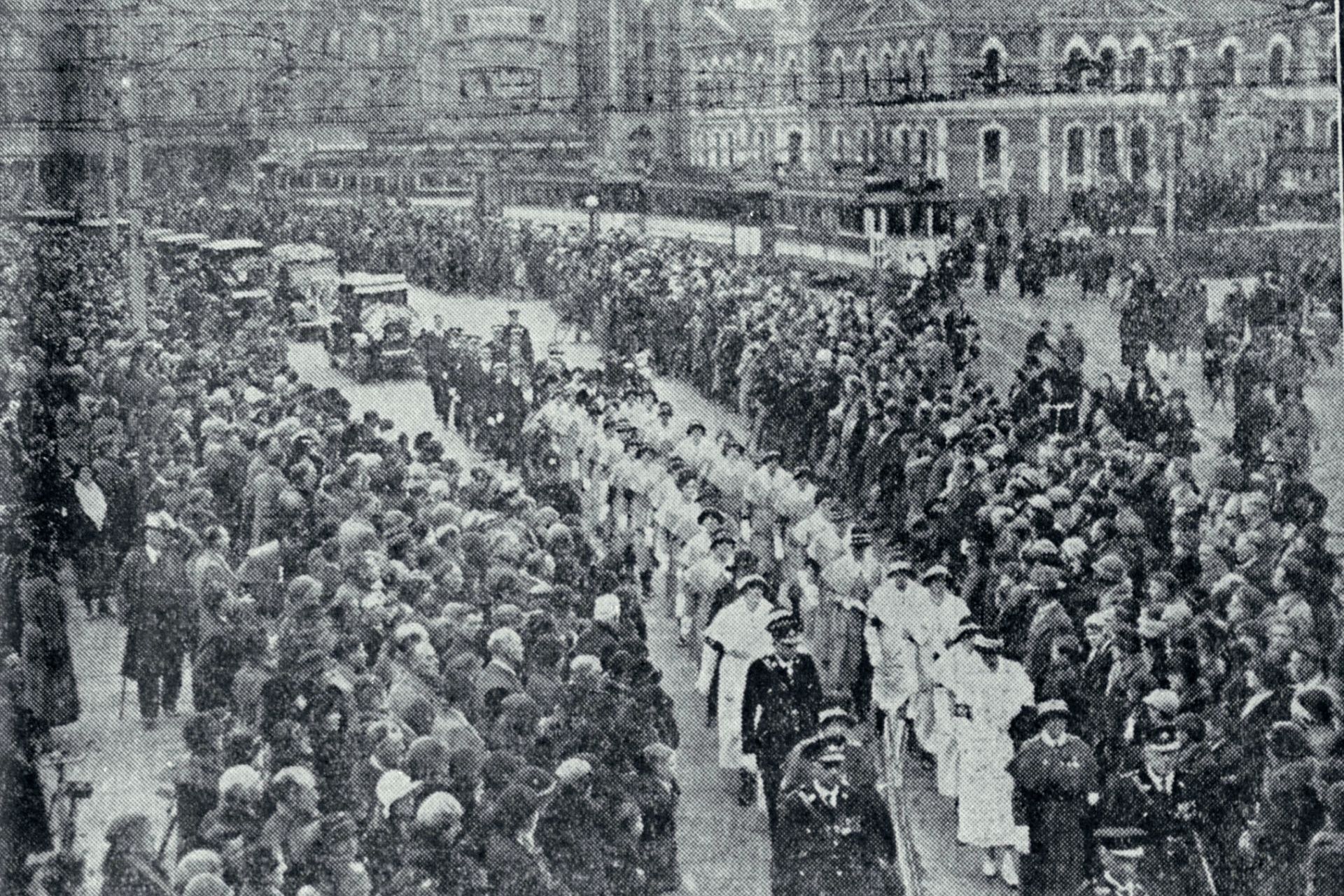 A black and white photo of a crowd of people walking down a street. - Nurse Maude