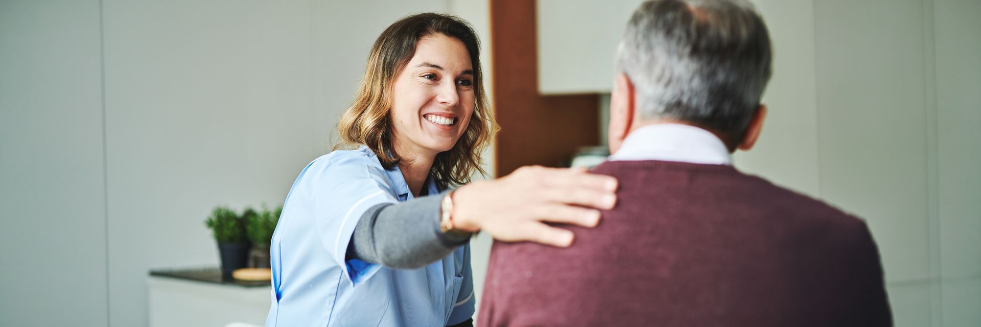 A woman in a blue uniform smiles at a man, placing her hand on his shoulder.
