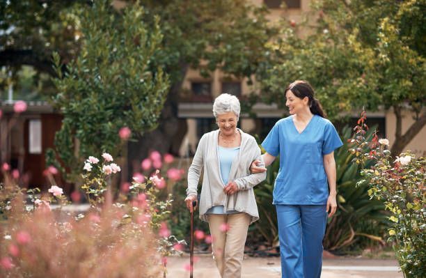 A nurse is helping an elderly woman walk in a park.