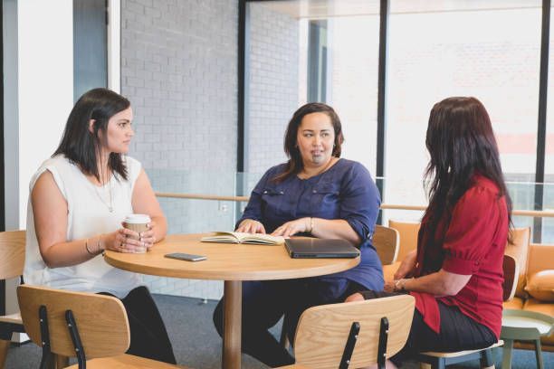 Three women are sitting at a table talking to each other.