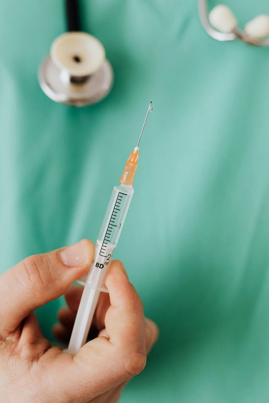 A person is holding a syringe in their hand in front of a stethoscope.