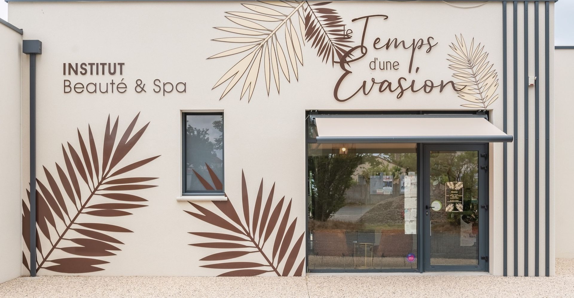 Extérieur de l'institut de beauté « Temps d'Une Évasion ». Façade beige ornée de feuilles de palmier brunes
