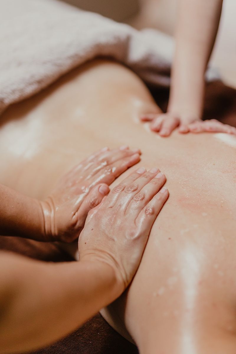 Mains massant le dos, appliquant de l'huile. Peau bronzée, gros plan.