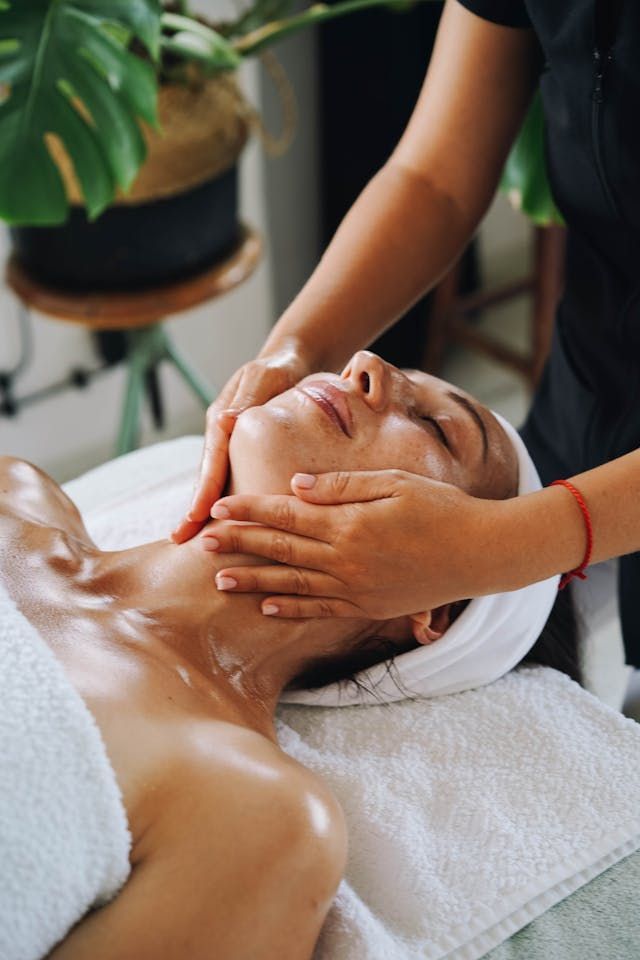Personne recevant un massage facial dans un spa ; les mains du thérapeute sur le visage et le cou.