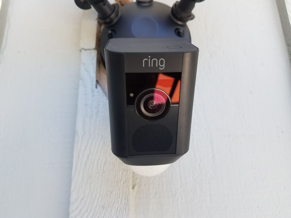 A black Ring floodlight camera mounted on a white exterior wall.