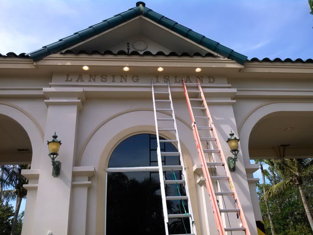 Two ladders lean against the ornate, cream-colored entrance to Lansing Island under a blue sky.
