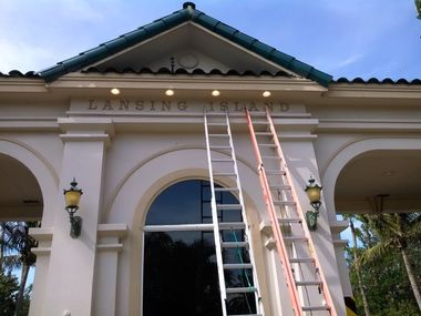 Two ladders lean against the ornate, cream-colored entrance to Lansing Island under a blue sky.