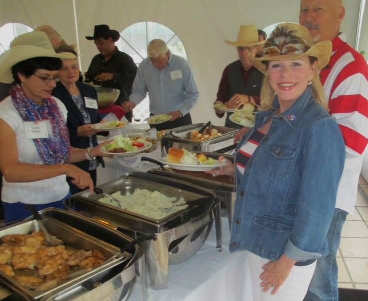 People at a buffet, wearing cowboy hats. They're serving themselves food from various heated trays in a tent.