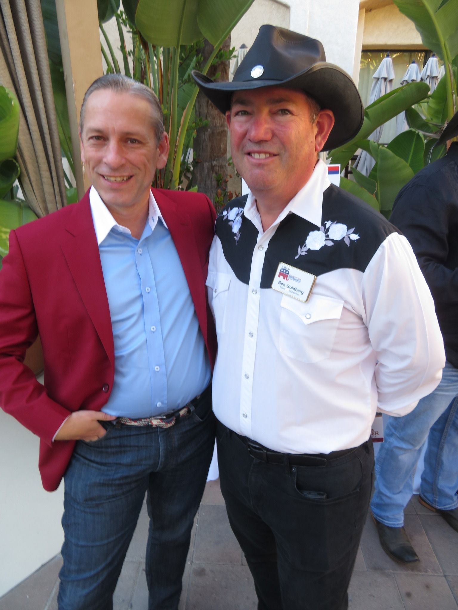 Three people smiling for a photo at an outdoor event; woman with arm around two men.