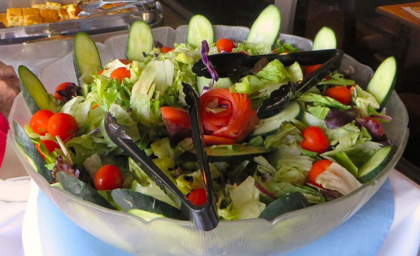 Salad bowl with lettuce, cucumbers, tomatoes, and salmon, with tongs.
