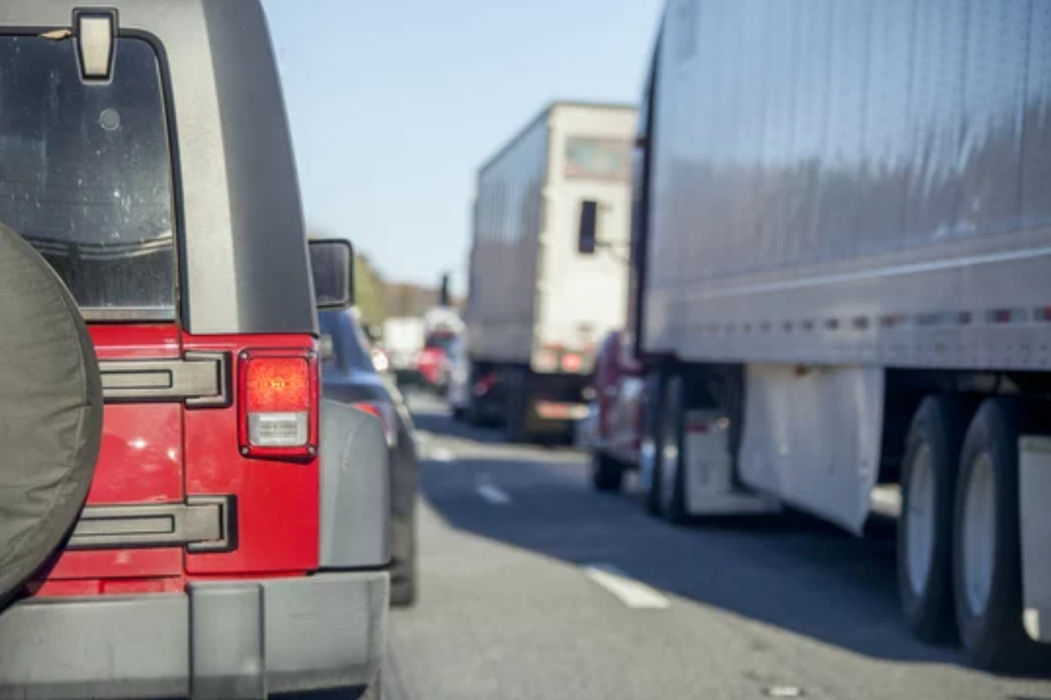 A red car driving alongside a semi-truck.