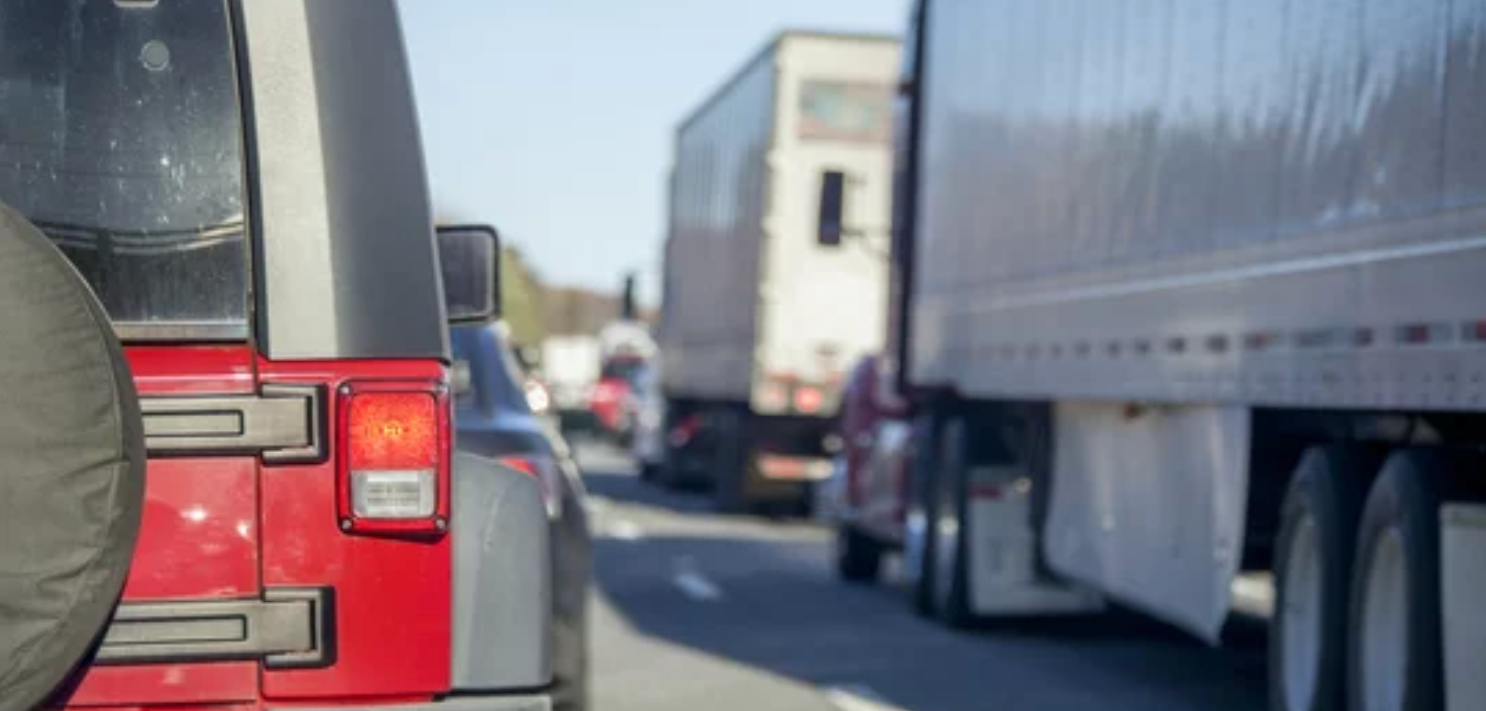 Photo of a red jeep driving alongside a semi truck on the road.