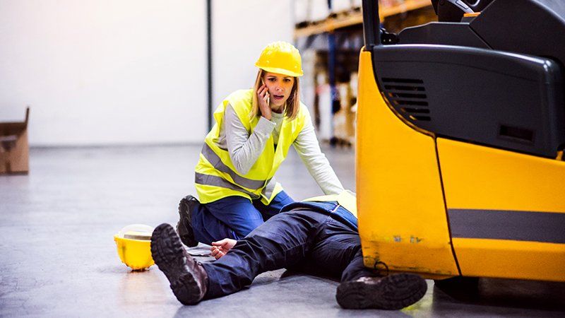 Woman in hard hat talks on the phone as someone lies unconscious next to her